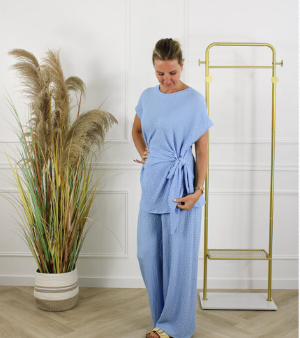 Hazel 2-delige dames set in lichtblauw met losvallende top voorzien van strikdetail en comfortabele wijde broek, gepresenteerd in een lichte studioomgeving. Trendy damesmode uit de collectie van DeNa Kids Boutique.