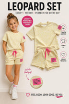 Gele luipaardprint kinderset bestaande uit een T-shirt en short met opvallende roze details, afgebeeld naast een model dat de outfit draagt. De zomerse set is gemaakt van zachte stof en verkrijgbaar in de maten 4, 6, 8, 10, 12 en 14 bij DeNa Kids Boutique.