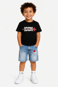Kindmodel draagt een zwart ICON T-shirt met witte opdruk en rode esdoornblad-details, gecombineerd met een lichtblauwe denim short met rode accenten. Trendy en comfortabele zomeroutfit voor kinderen, geschikt voor dagelijks gebruik en casual gelegenheden. Beschikbaar in de maten 4, 6, 8, 10, 12 en 14.