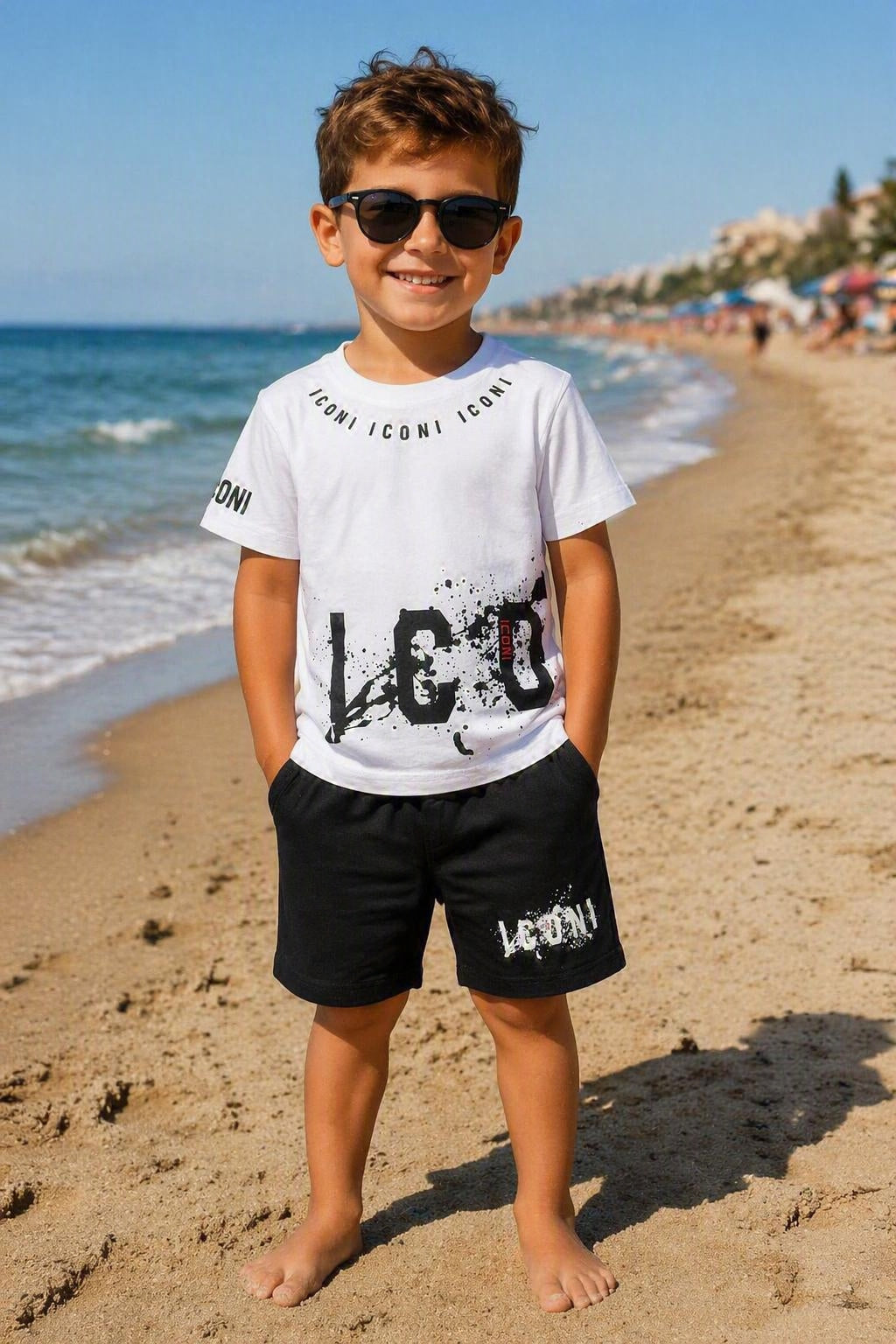 Kindermodel op het strand met een wit Iconi T-shirt en zwarte short uit de zomercollectie voor kinderen, comfortabele zomer set verkrijgbaar in maten 4 tot en met 14 jaar.