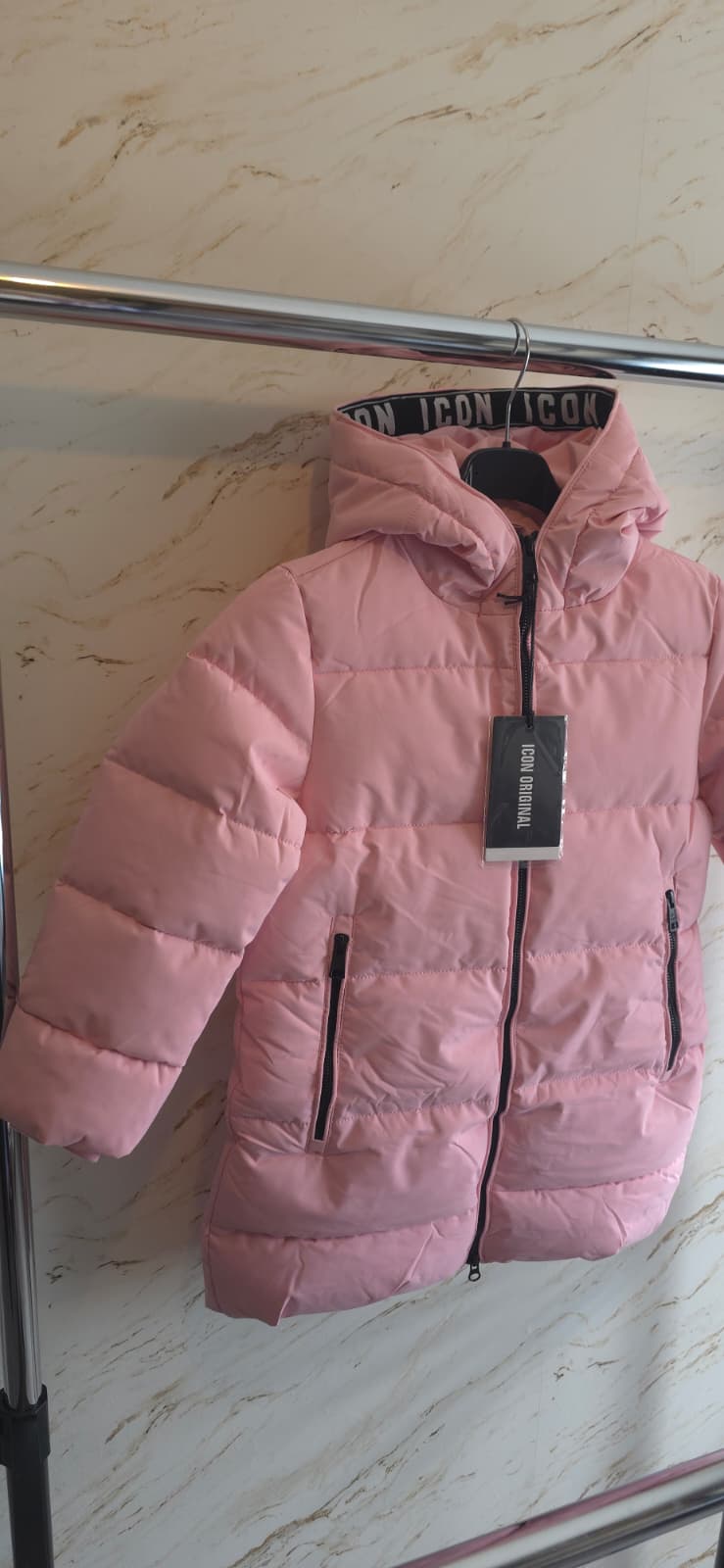 Roze gewatteerde winterjas voor meisjes van ICON met capuchon, ritssluiting en warme voering, hangend aan een kledingrek.