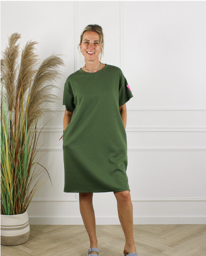 Life Label Army Green damesjurk met korte mouwen en rechte pasvorm, gefotografeerd in een lichte studio met decoratieve siergrassen. Comfortabele groene casual jurk uit de dameskledingcollectie van DeNa Kids Boutique.