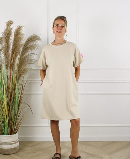 Beige damesjurk van Life Label met korte mouwen en rechte pasvorm, gepresenteerd in een lichte studioomgeving met decoratieve siergrassen, onderdeel van de dameskledingcollectie van DeNa Kids Boutique.