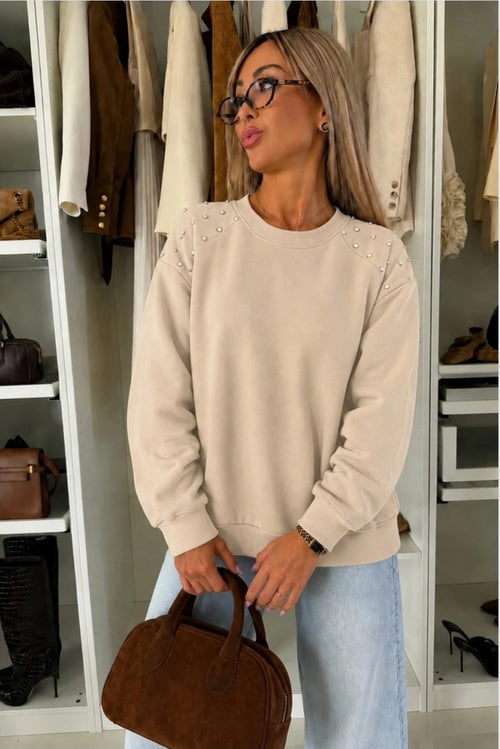 Beige dames sweater met pareldetails op de schouders, lange mouwen en ronde hals gecombineerd met een lichtblauwe jeans 