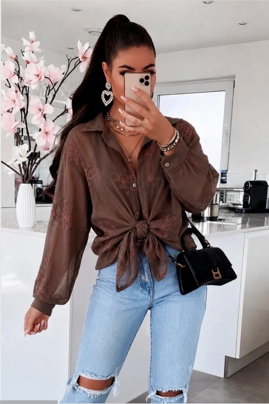 Bruine dames blouse met borduurwerk, lange mouwen en knoopsluiting, gestyled met een lichtblauwe jeans en zwarte handtas.
