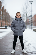 Jongen van 8-10 jaar draagt grijze gewatteerde ICON puffer winterjas met capuchon en ICON logo op de rits in een urban buitenomgeving