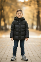 Jongen in zwarte ICON gewatteerde winterjas met New Balance 9060 sneakers en donkerblauwe jeans, lifestyle bokeh achtergrond - DeNa Fashion