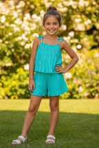 Meisjes turquoise zomerset met gelaagde ruche top en short met witte sandalen - model 2 - tuin achtergrond | DeNa Fashion