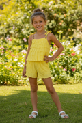 Meisjes gele zomerset met gelaagde ruche top en short met witte sandalen - model 2 - tuin achtergrond | DeNa Fashion