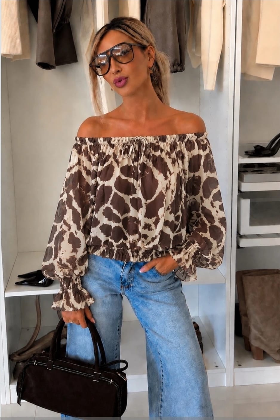 Off-shoulder dames top met bruine print, lange ballonmouwen en elastische halslijn gecombineerd met een lichtblauwe jeans