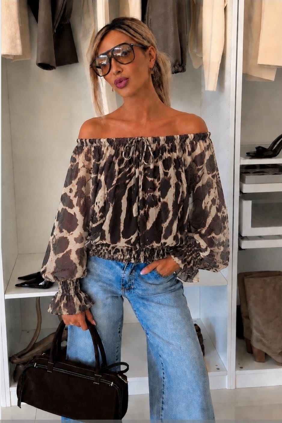 Off-shoulder dames top met bruine dierenprint, lange ballonmouwen en elastische halslijn gecombineerd met een lichtblauwe jeans.