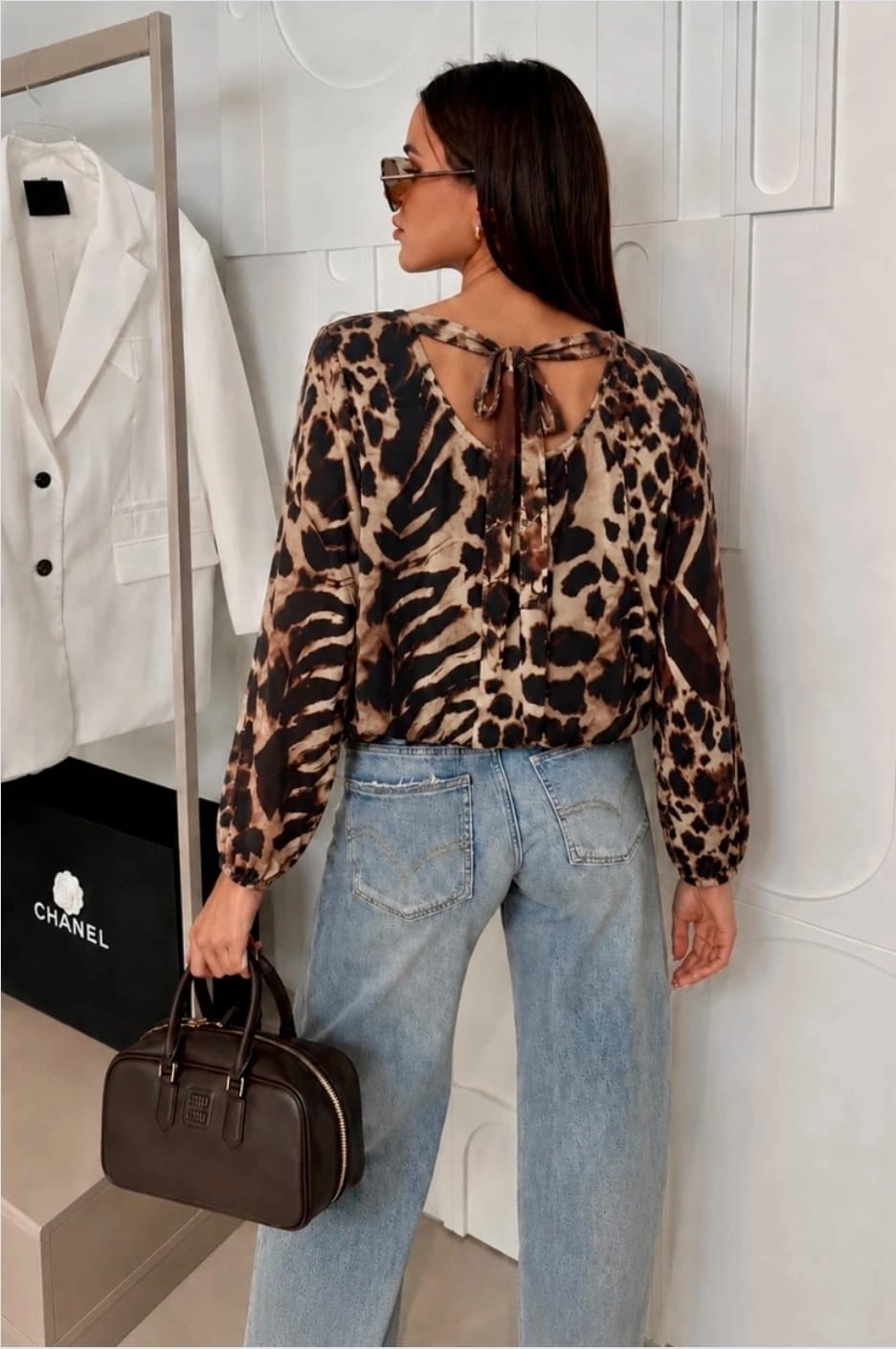 Rugzijde van een dames panterprint top met lange mouwen, strikdetail in de nek en losvallende pasvorm gecombineerd met een lichtblauwe jeans.