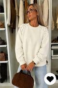 Witte dames sweater met parel details op de schouders, ronde hals en lange mouwen gecombineerd met een lichtblauwe jeans.